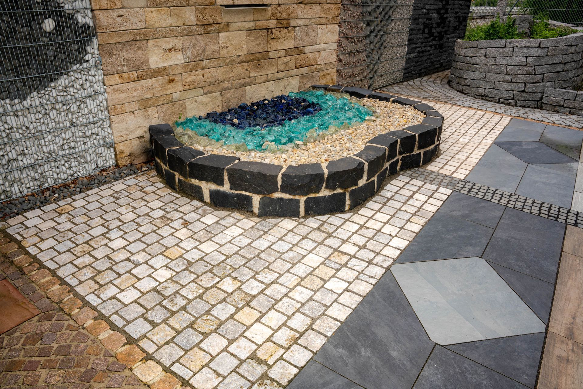 Pflasterfläche mit Natursteinmosaik und rundem Brunnen im Garten