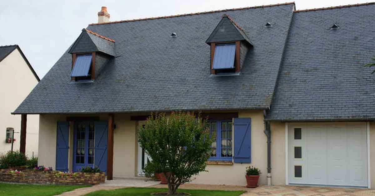 Maisonnette avec un toit en ardoise gris foncé, des volets bleus et une porte de garage blanche.