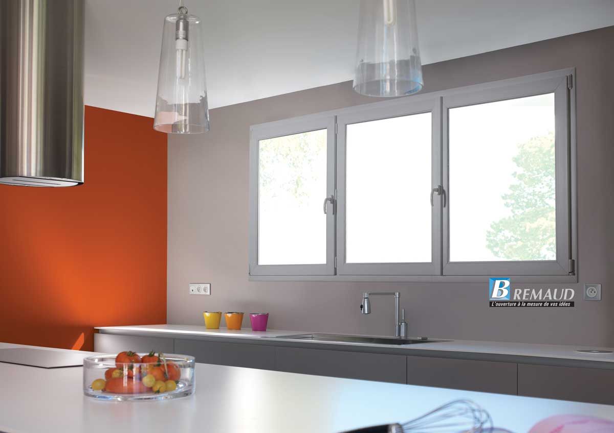 Cuisine moderne avec un plan de travail blanc, un mur orange, une triple fenêtre et une hotte en acier inoxydable.