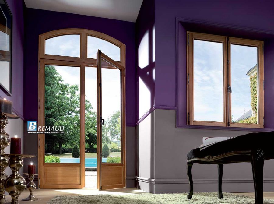 Portes-fenêtres et fenêtre à cadre en bois dans une pièce aux murs violets, donnant sur un jardin ensoleillé.