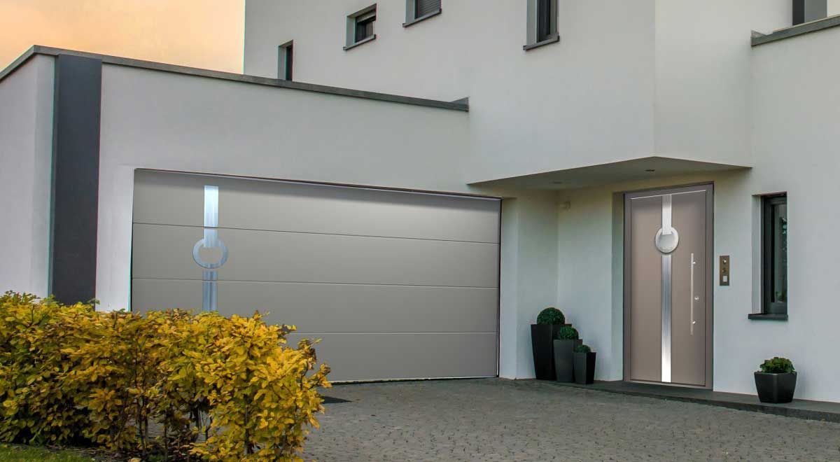 Maison blanche moderne avec porte de garage et porte d'entrée grises, arbustes devant.