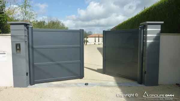 Portail d'allée en métal gris, ouvert, avec des piliers de chaque côté.