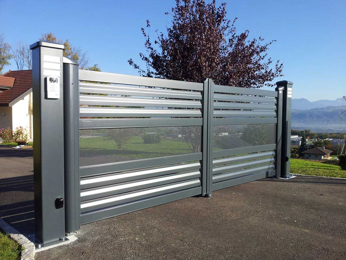 Portail d'allée en métal gris avec lattes horizontales et deux poteaux de soutien ; allée pavée.
