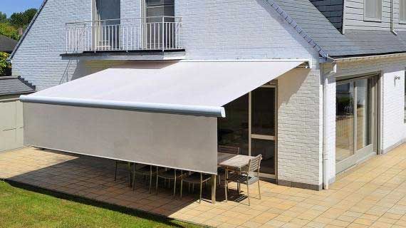 Auvent rétractable blanc au-dessus du mobilier de terrasse extérieur, à côté d'une maison blanche.