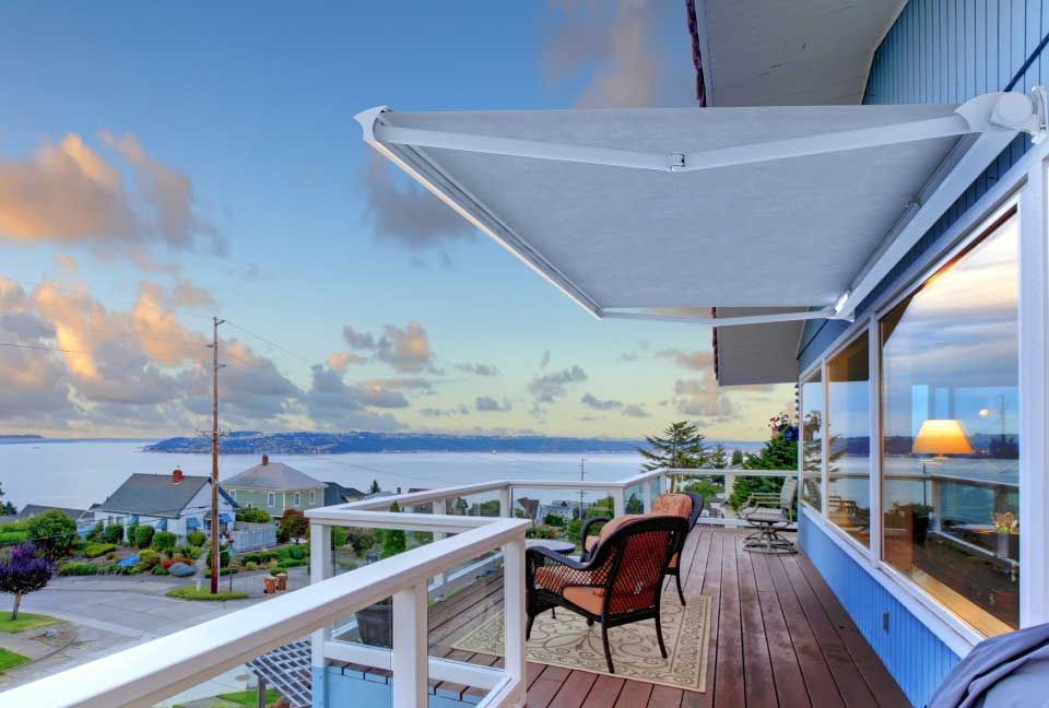 Terrasse avec auvent rétractable donnant sur l'eau et la ville, bois brun, maison bleue.