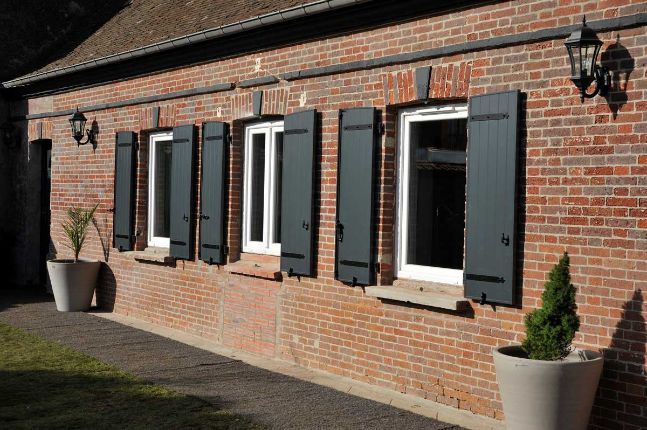 Bâtiment en briques rouges avec des volets noirs aux fenêtres à cadre blanc, deux jardinières flanquent le mur.