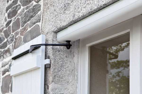 Volets blancs sur un bâtiment en pierre avec un bras de soutien noir.
