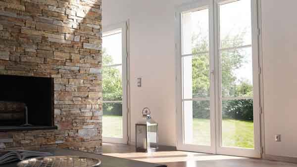 Salon avec portes à cadre blanc, cheminée en pierre et vue sur un jardin ensoleillé.