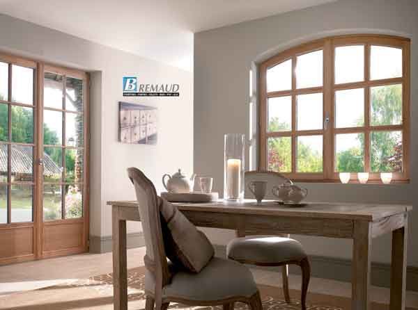 Salle à manger avec table en bois, chaises, fenêtre cintrée et portes-fenêtres donnant sur un jardin.