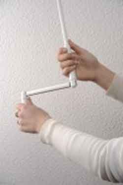 Des mains actionnent une manivelle blanche fixée au plafond, probablement pour ouvrir ou fermer une fenêtre ou un store.