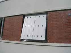 Volet blanc recouvrant une fenêtre, encastrée dans un mur de briques.