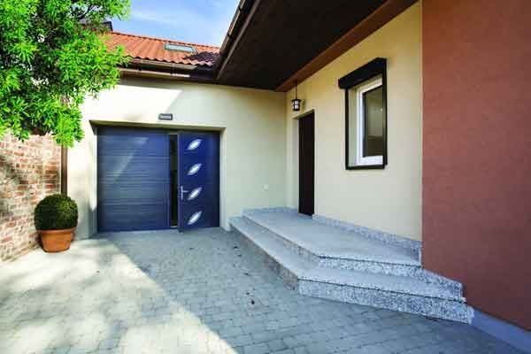 Entrée de garage avec porte bleue, marches, allée et petite fenêtre sous un toit.