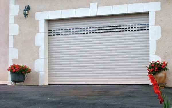 Porte de garage sectionnelle beige à cadre en pierre, avec jardinières de chaque côté, installée sur une allée.