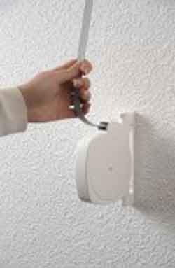 Tirage manuel d'un fil à linge rétractable enroulé sur un enrouleur blanc fixé au mur.