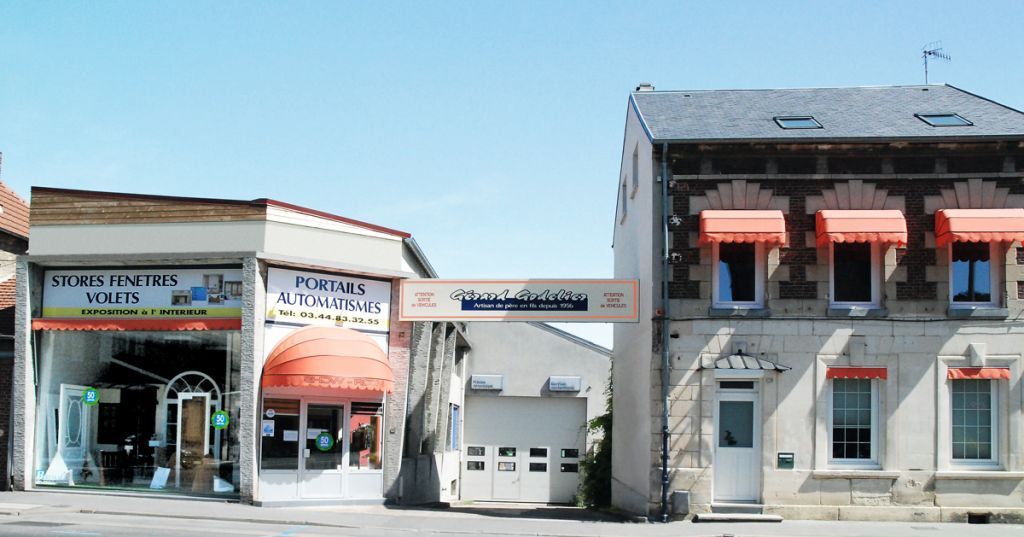 Des boutiques alignées avec des auvents. Comprend une porte de garage, le tout sous un ciel bleu.