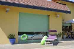 Bâtiment jaune avec un store vert à une fenêtre. Des jouets de piscine et une chaise se trouvent devant le bâtiment.