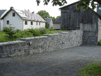 Natursteinmauer an einem Weg und zwei Häuser im Hintergrund