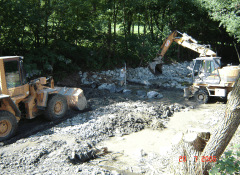 Bauarbeiten an einer Fischtreppe mit Baggern an einem Fluss in einem Waldgebiet