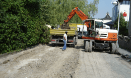 Wegebau mit orangefarbenem Bagger, der Schutt in einen Kleinlaster hebt