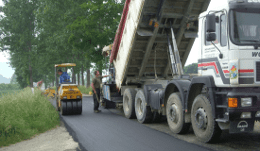 kleine gelbe Planierraupe und Lkw mit gekippter Ladefläche auf einer sanierten Straße