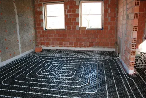 Una habitación con una pared de ladrillo y un sistema de calefacción por suelo radiante negro.