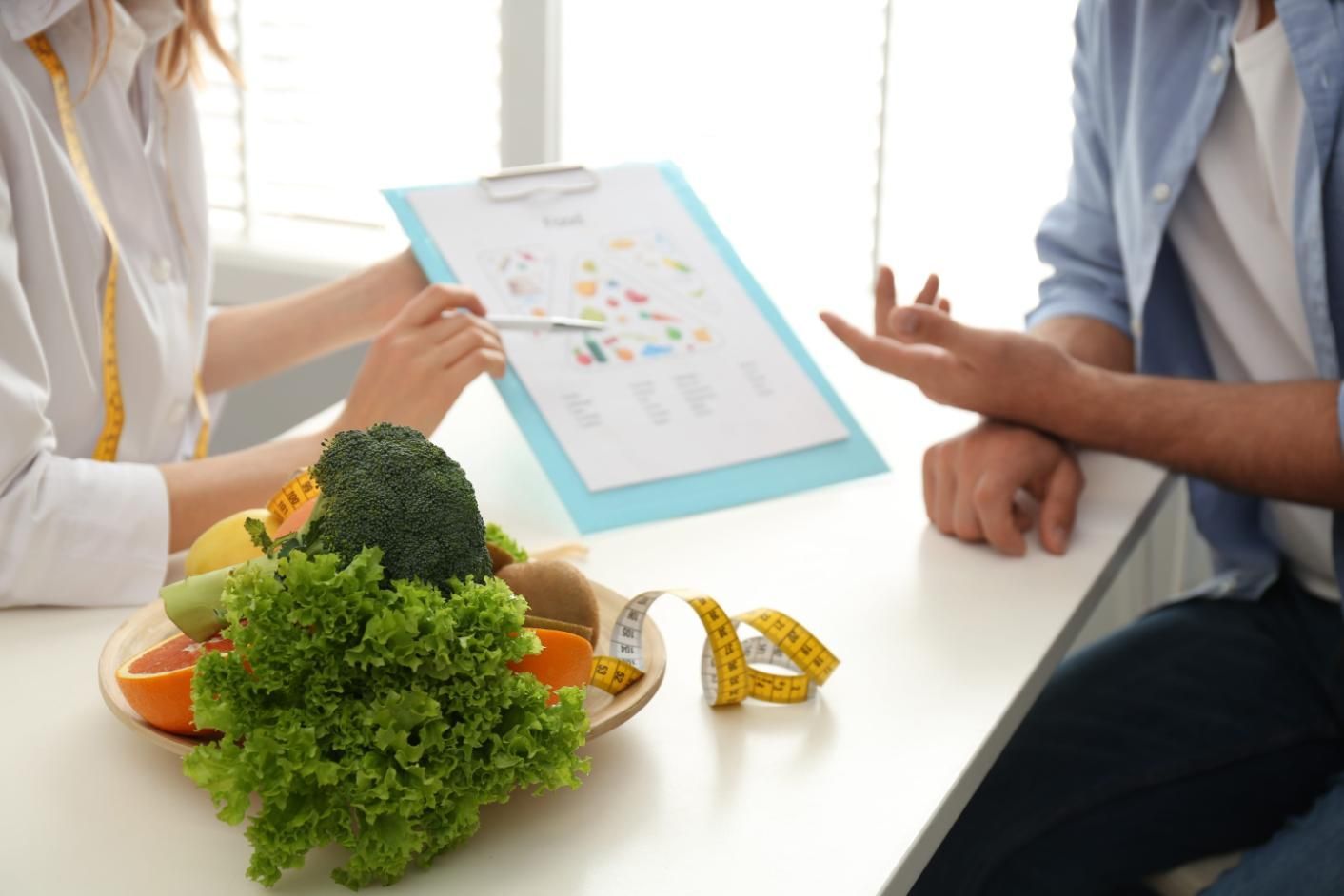 Consulta nutricional con verduras y una tabla de alimentos en una mesa.