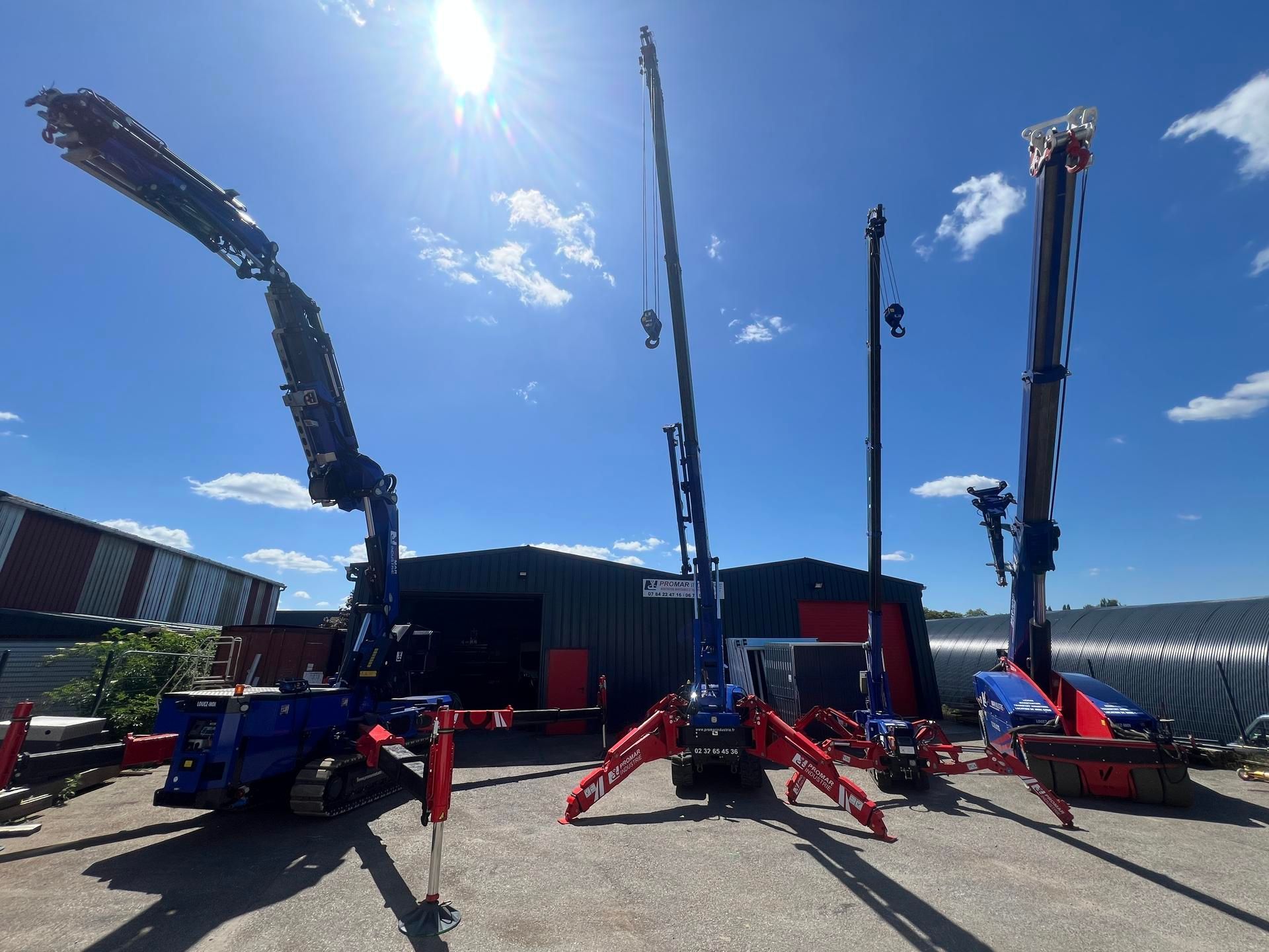 De hautes grues de chantier bleues se dressent sur un site industriel en plein air, sous un ciel d'un bleu éclatant.
