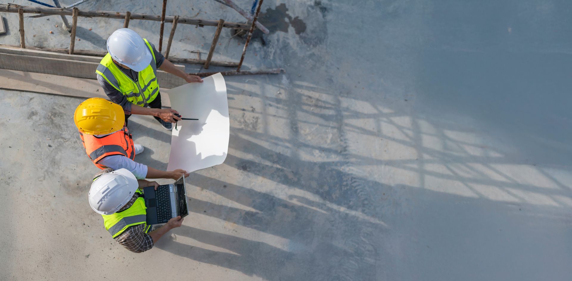 Des ouvriers du bâtiment examinent des plans sur un chantier, portant des casques et des gilets de sécurité jaunes.