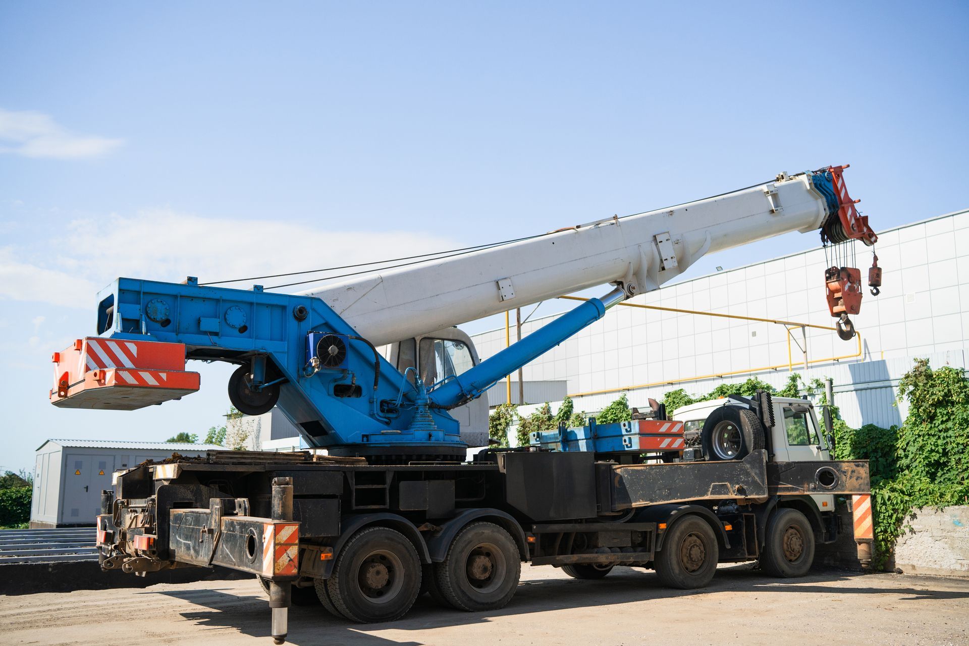 Grue mobile bleue et blanche à flèche déployée, stationnée à l'extérieur.