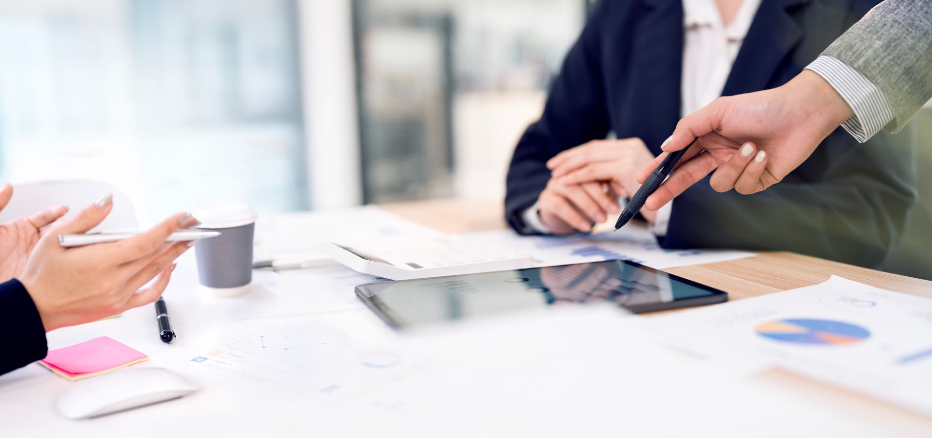 Des personnes en tenue professionnelle assises à une table discutent de documents et utilisent une tablette.