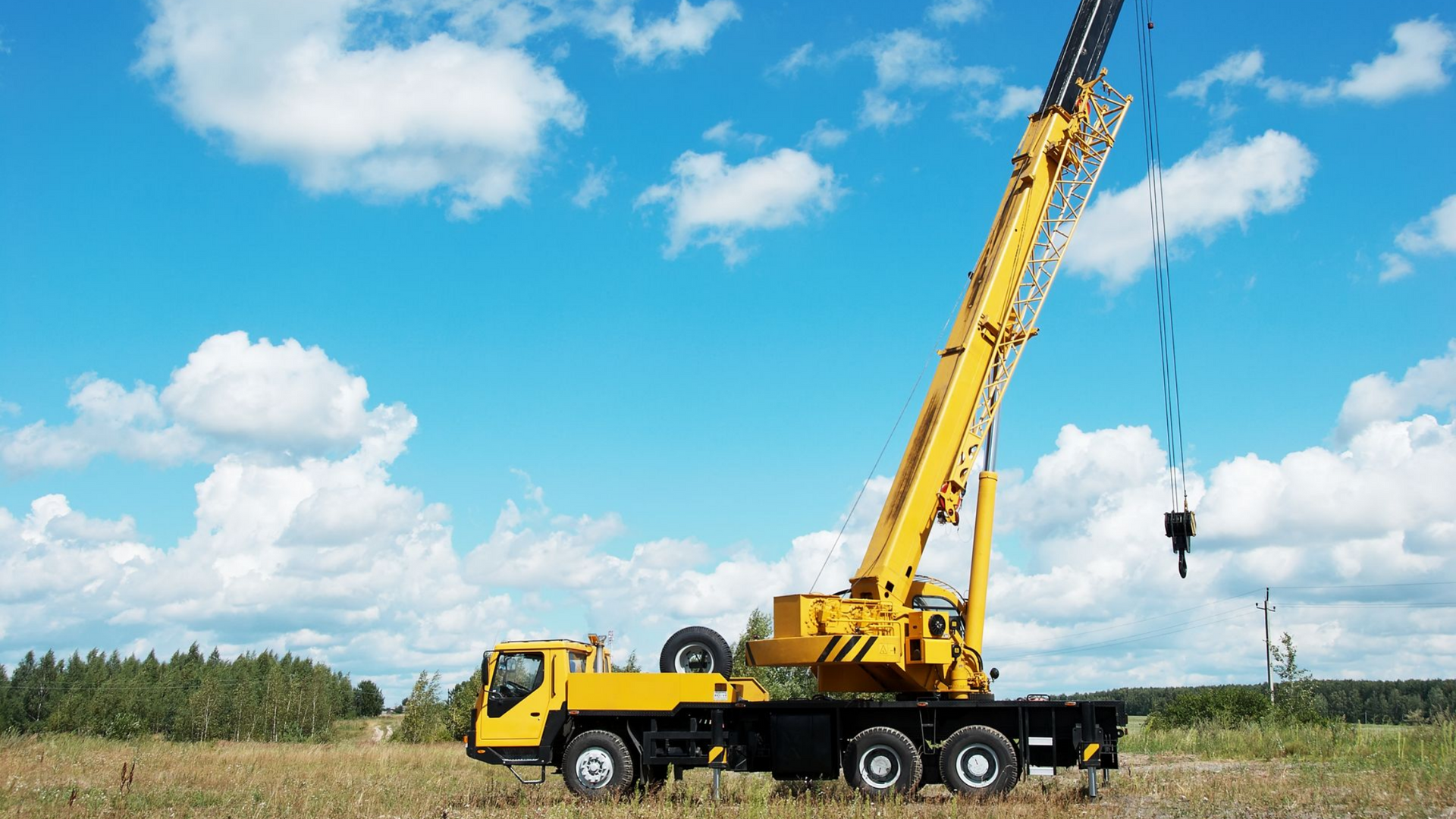 Grue mobile jaune dans un champ sous un ciel bleu parsemé de nuages blancs duveteux.