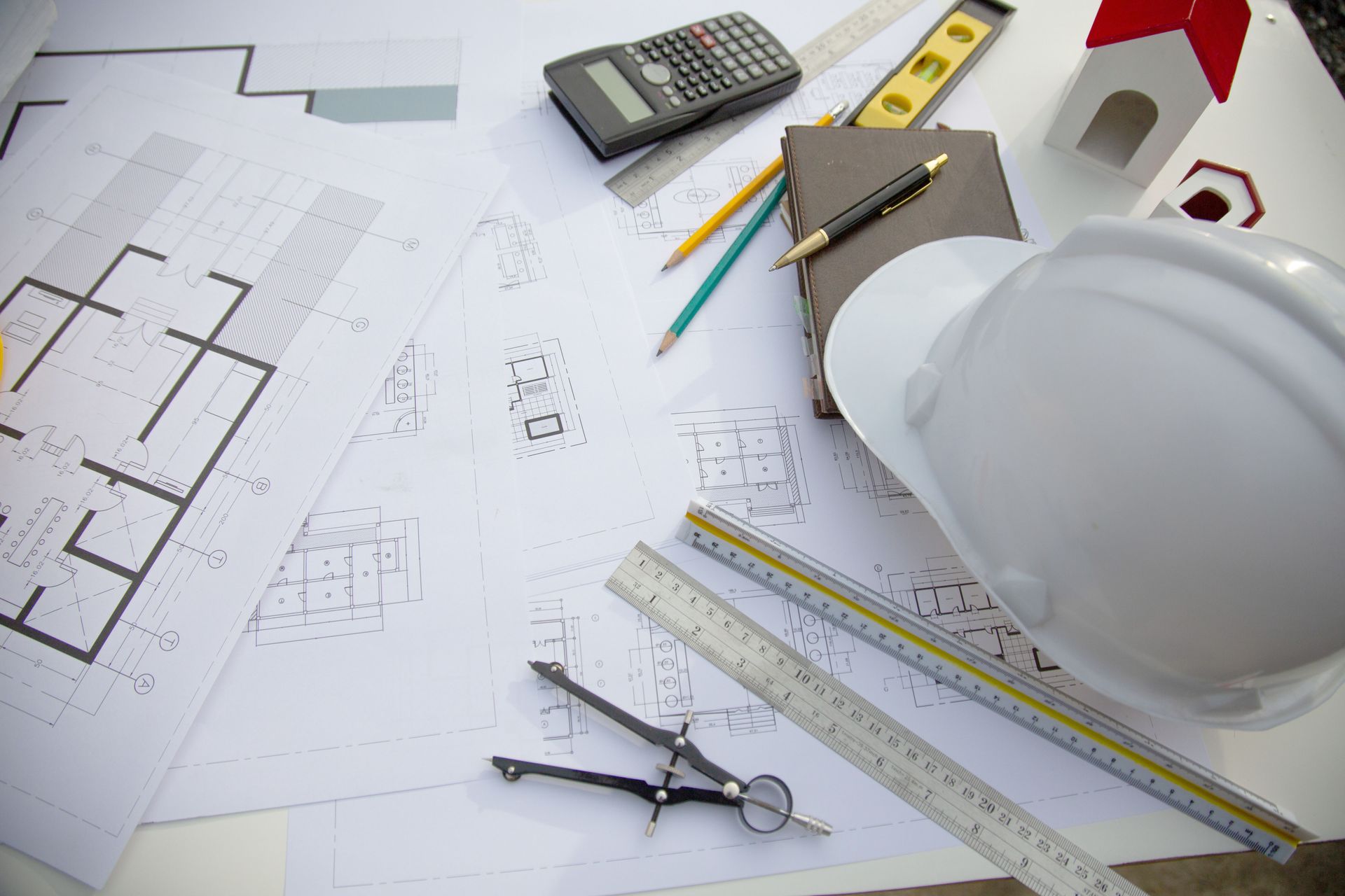 Plans d'architecte et outils, notamment une calculatrice, un niveau et un casque de chantier.