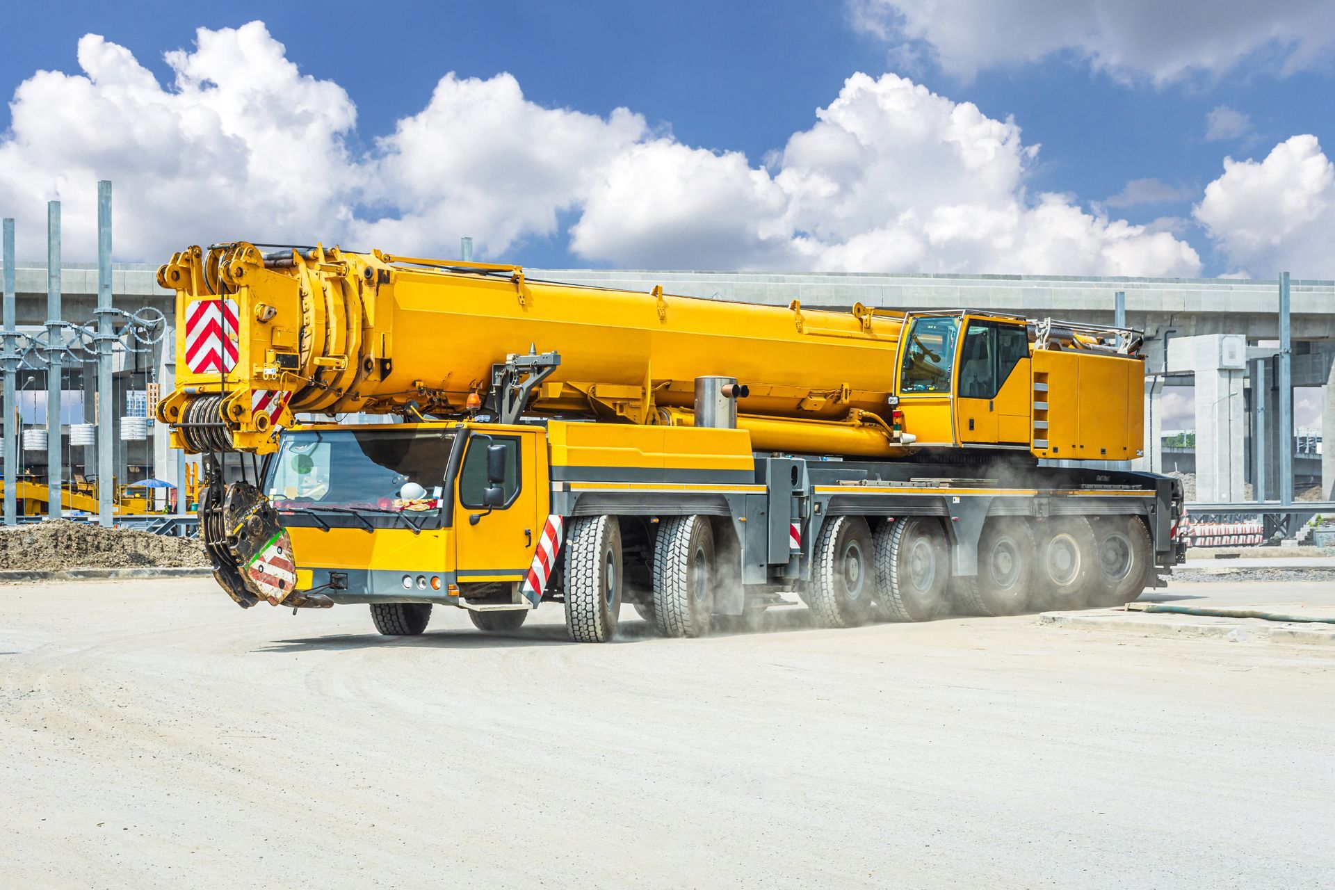 Grue mobile jaune sur une surface poussiéreuse, flèche levée, ciel blanc et bleu.