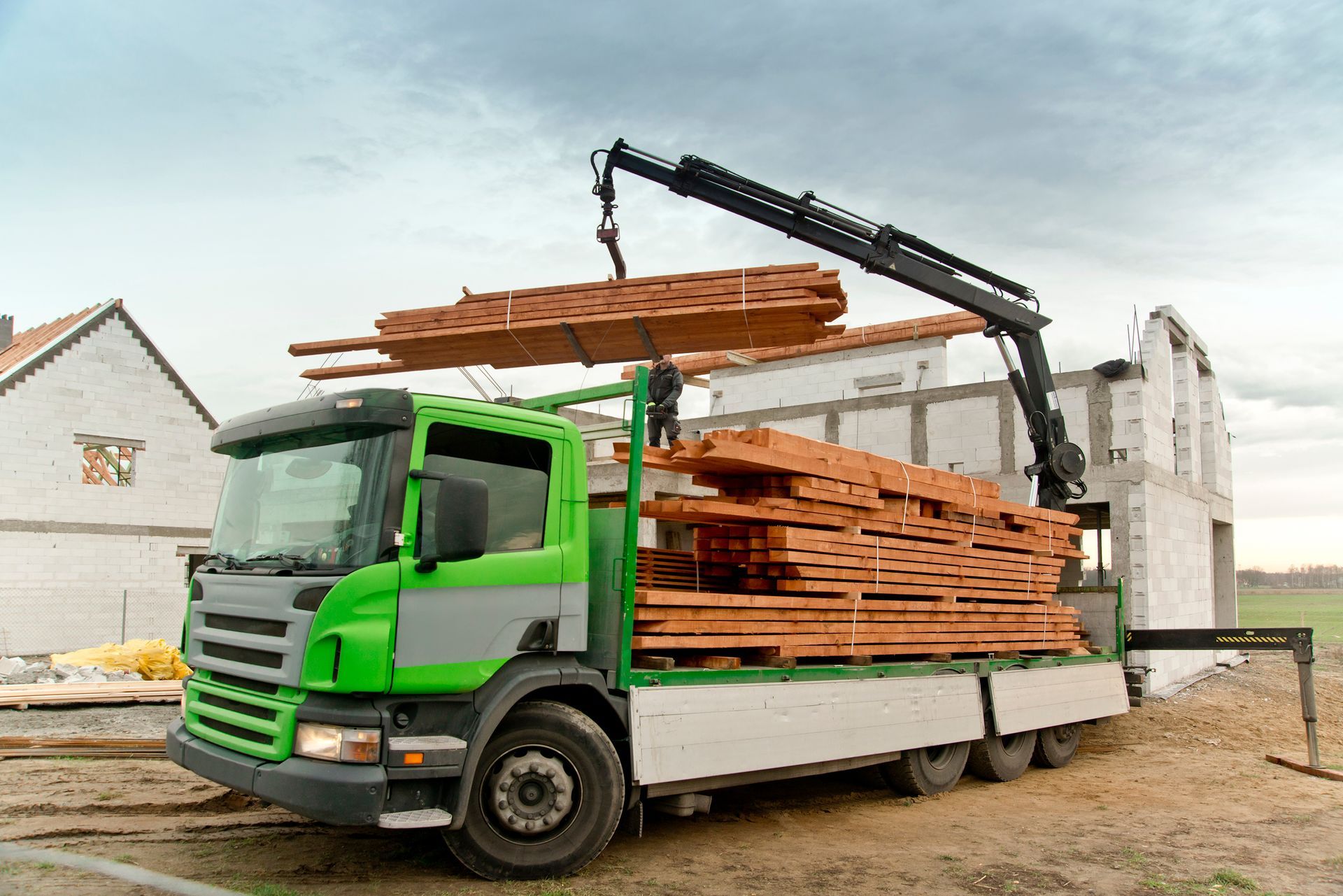 Un camion vert décharge du bois sur un chantier de construction à l'aide d'une grue.