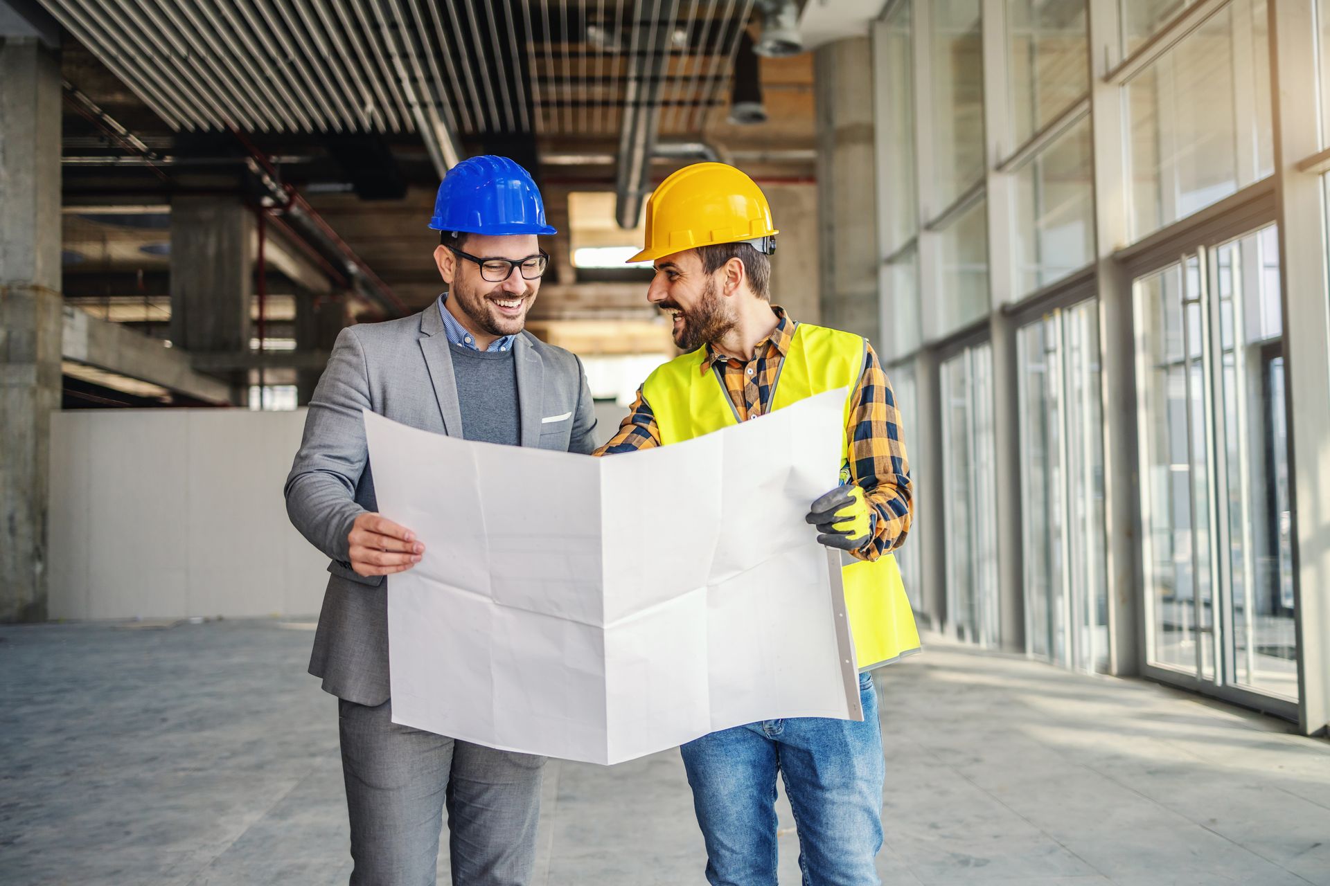 Deux ouvriers du bâtiment, casques de chantier sur la tête, examinent les plans d'un immeuble en construction.