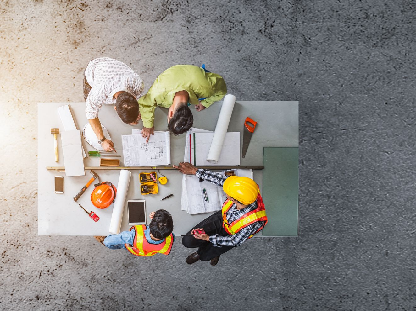 Vue aérienne : Une équipe de construction autour d'une table avec des plans, des outils et un ordinateur portable.