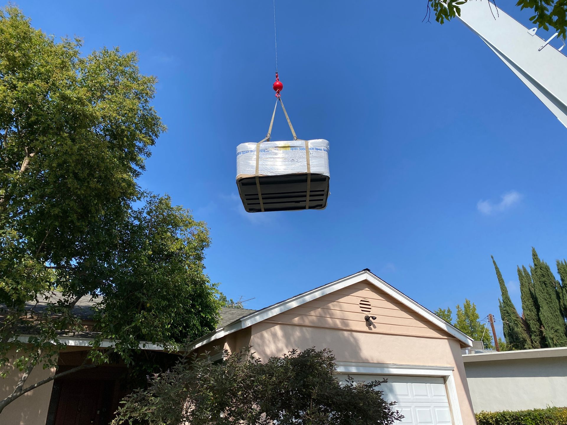 Une grue soulève un système de climatisation préfabriqué au-dessus d'une maison par une journée ensoleillée.