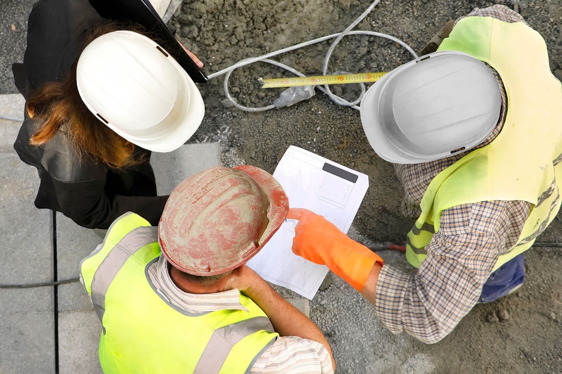 Trois ouvriers du bâtiment, casqués, examinent un document sur un chantier.