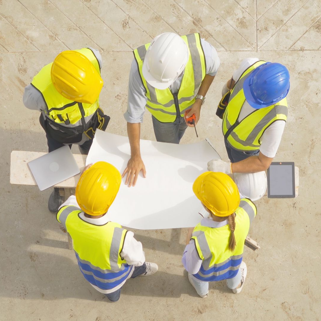 Des ouvriers du bâtiment, casqués et vêtus de gilets de sécurité, examinent les plans sur le chantier.
