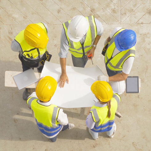 Des ouvriers du bâtiment, casqués et vêtus de gilets de sécurité, examinent les plans sur le chantier.