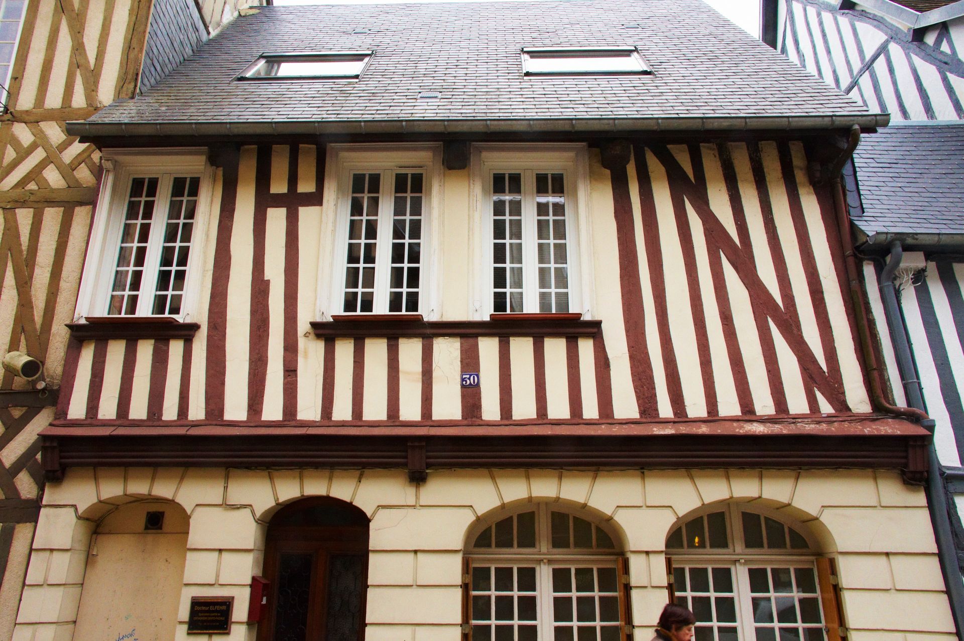 Bâtiment à ossature bois de deux étages, avec un rez-de-chaussée clair et des étages supérieurs bruns et blancs ; fenêtres cintrées.