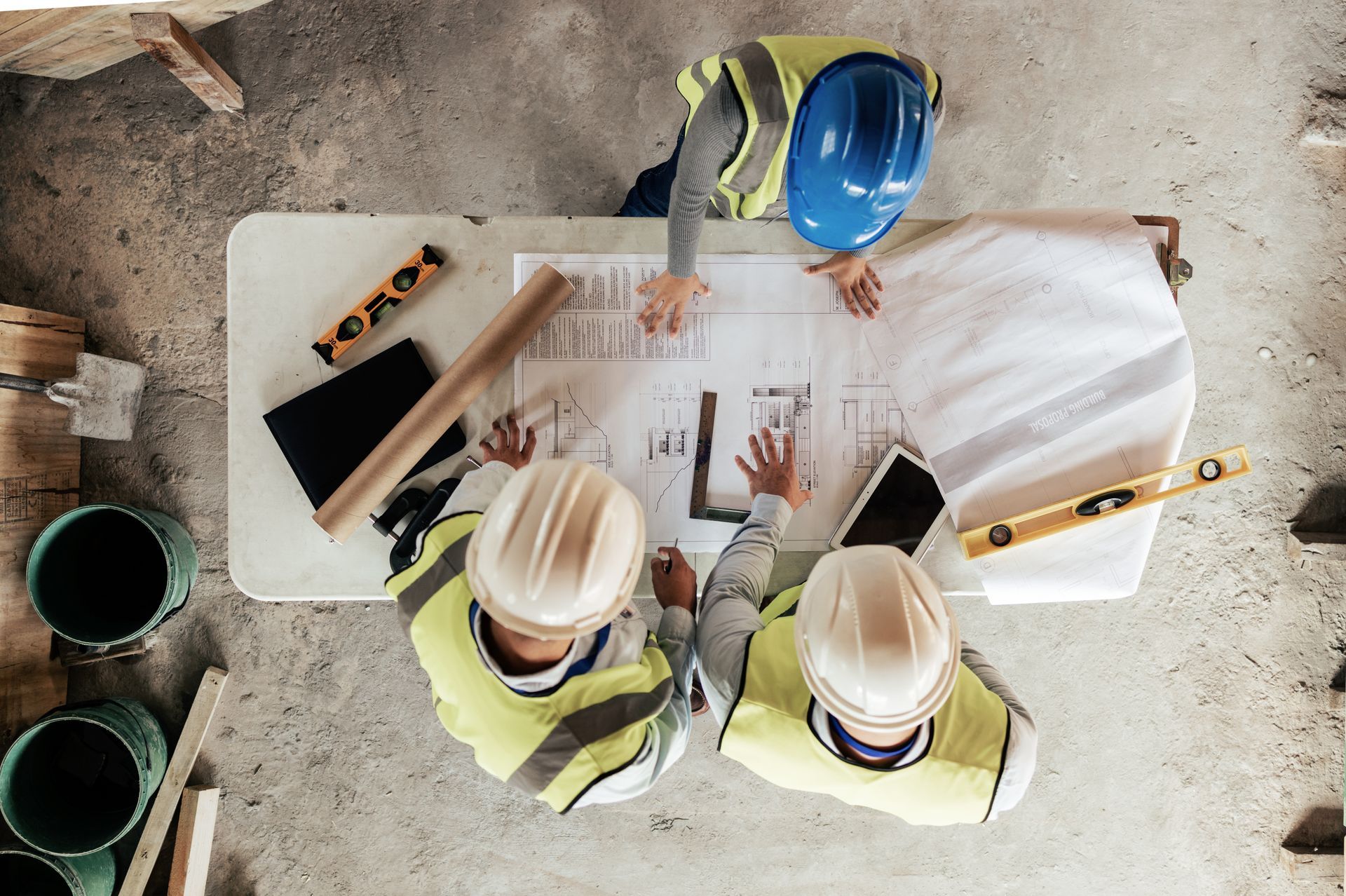 Des ouvriers du bâtiment, vêtus de gilets et de casques de chantier, examinent des plans sur une table.