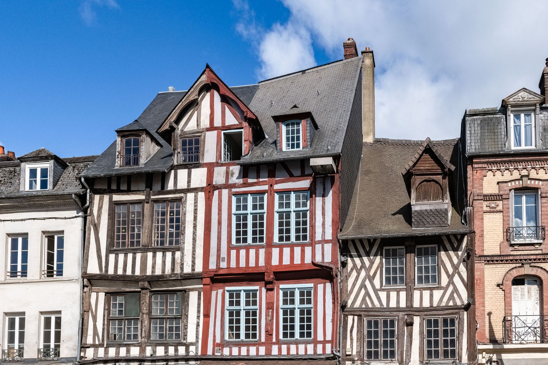Rangée de bâtiments à colombages avec des touches de bois rouge et brun, sous un ciel bleu.