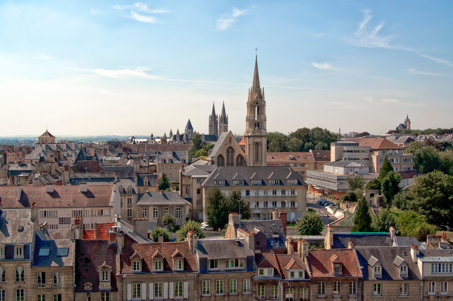 Vue de la ville avec le clocher d'une église sous un ciel bleu, des toits de tuiles rouges et des bâtiments en pierre.