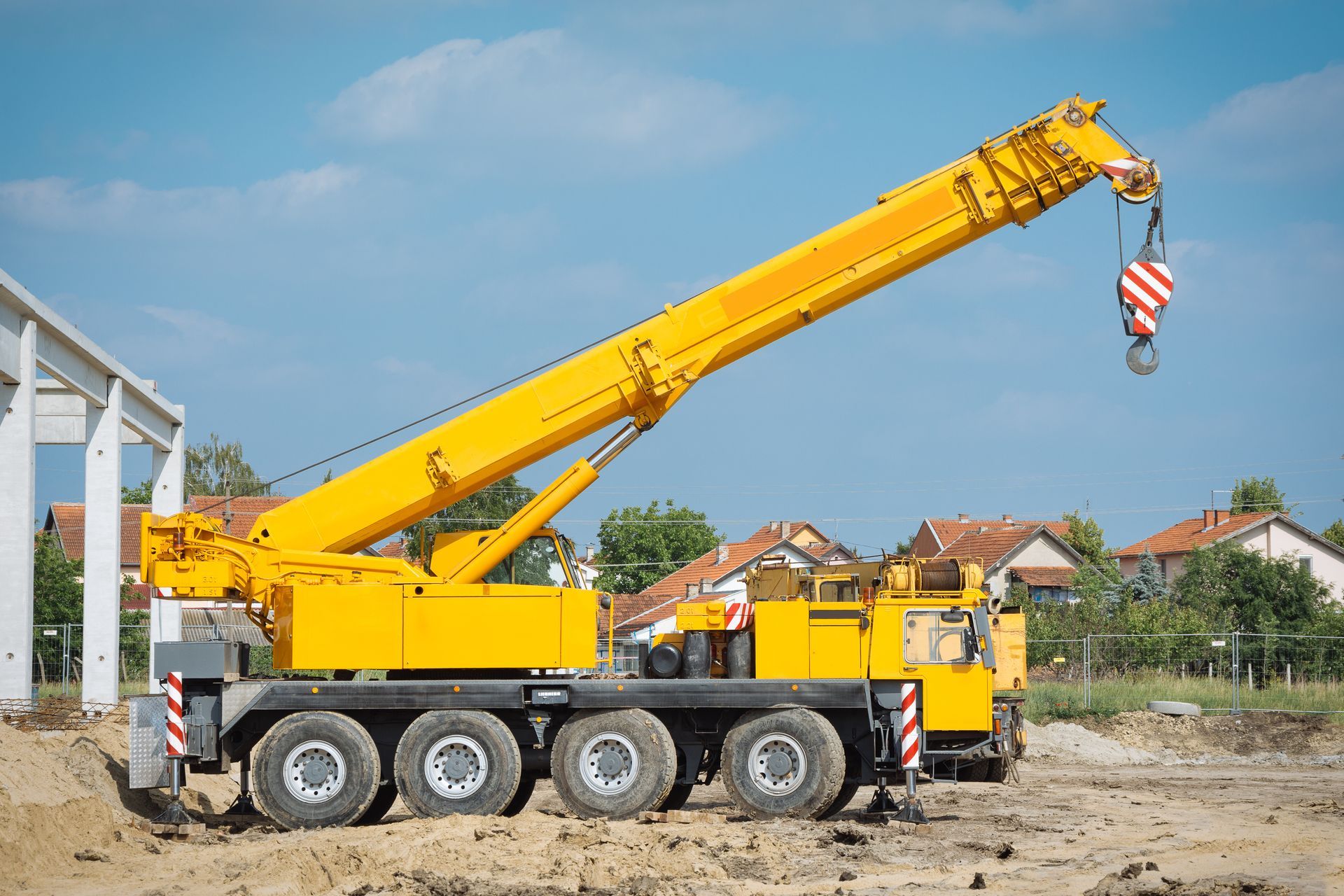 Grue mobile jaune à flèche déployée sur un chantier de construction, sur fond de ciel bleu.