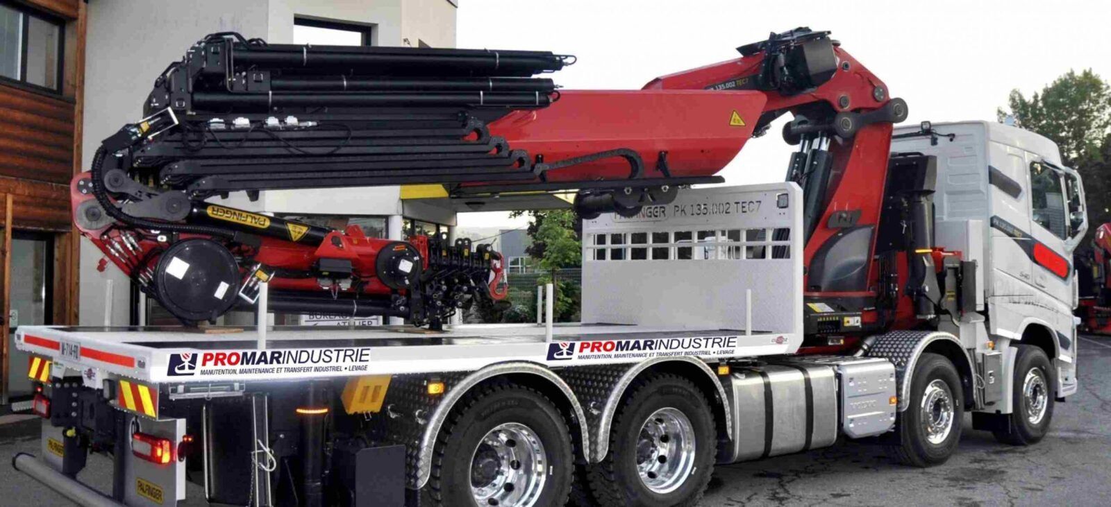 Un camion-grue équipé d'un bras de grue rouge et noir est stationné à l'extérieur, arborant le logo d'une entreprise sur le côté.