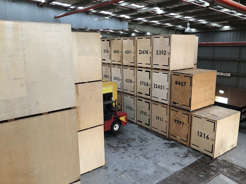 Un chariot élévateur dans un entrepôt rempli de caisses en bois, certaines numérotées.