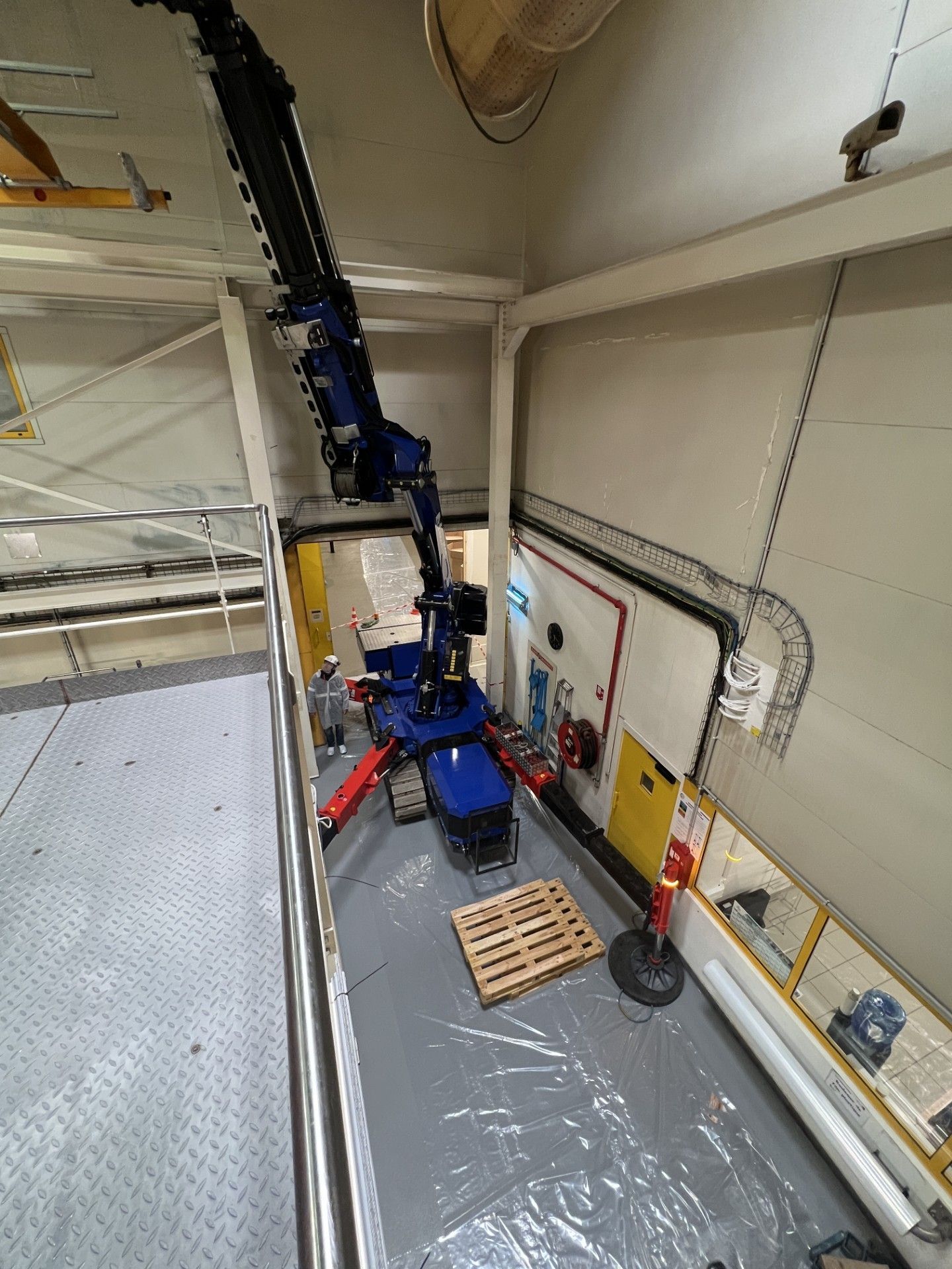Bras de robot industriel dans un coin d'entrepôt, à côté d'une palette et de barrières de sécurité.