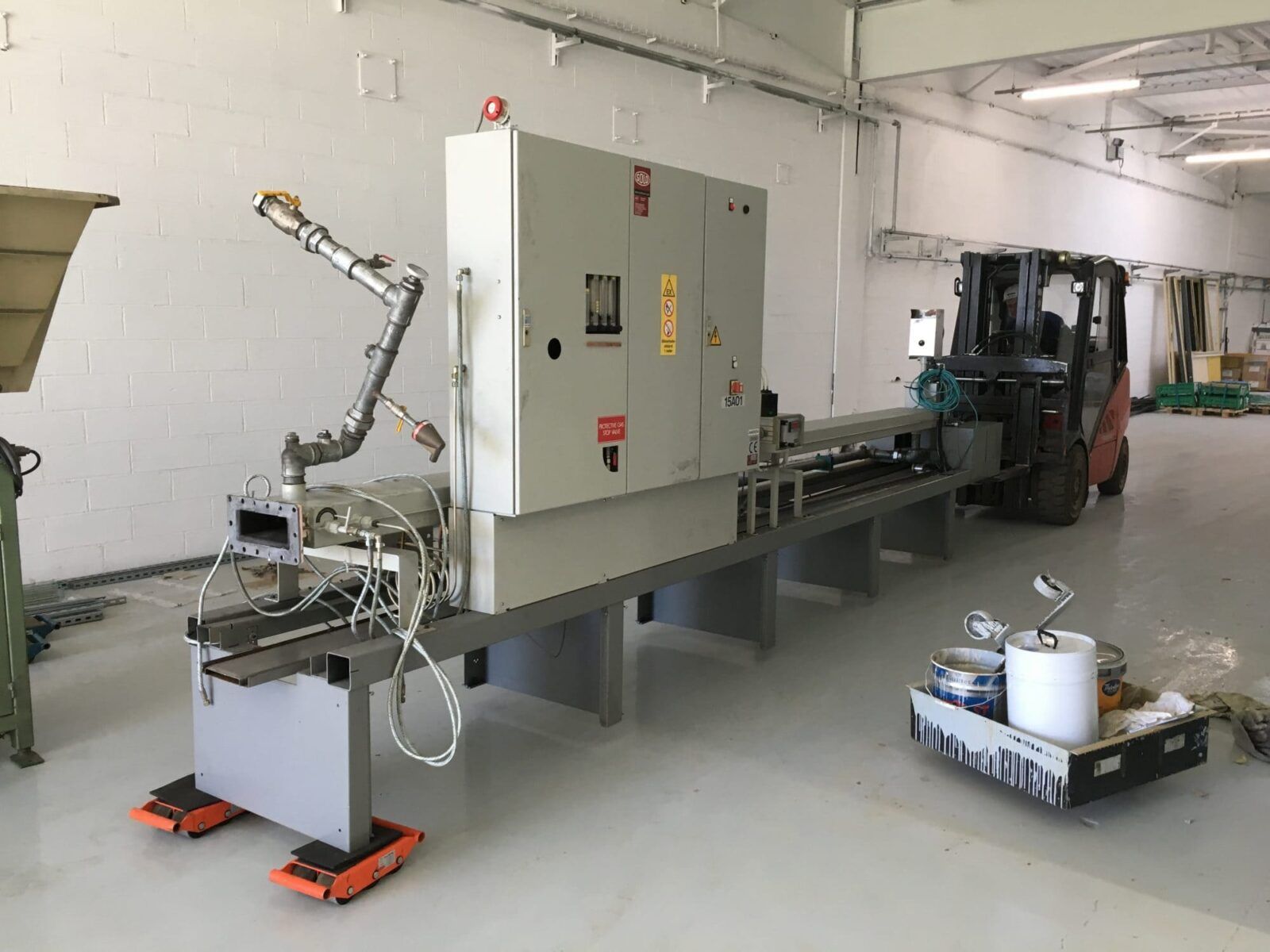 Longue machine industrielle avec panneau de commande et chariot élévateur dans un environnement d'usine.