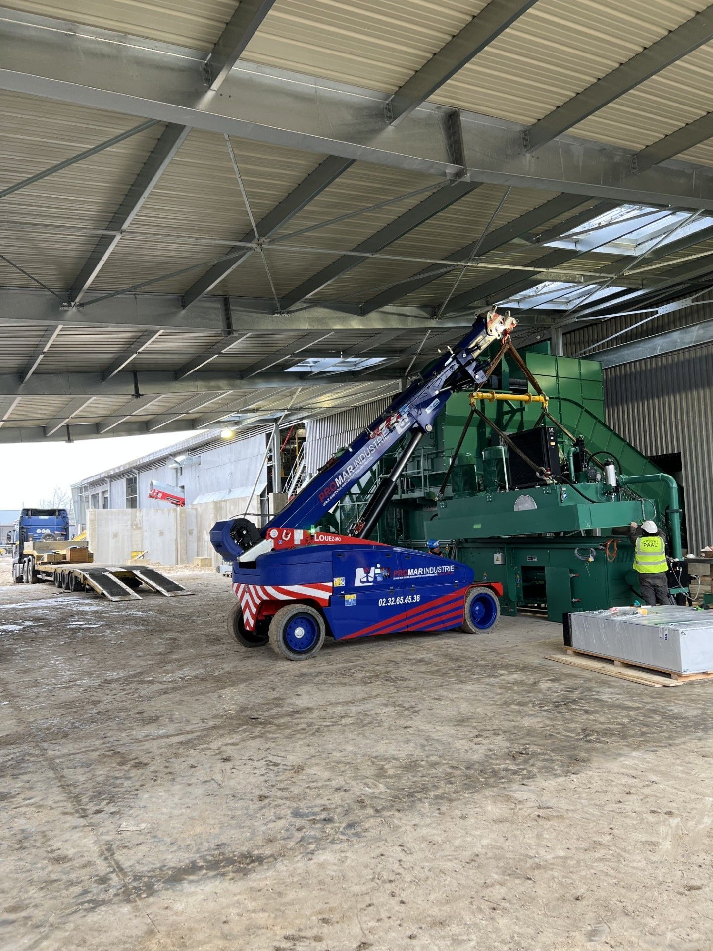 Un chariot élévateur rouge et bleu à côté d'une grosse machine verte dans un entrepôt en construction
